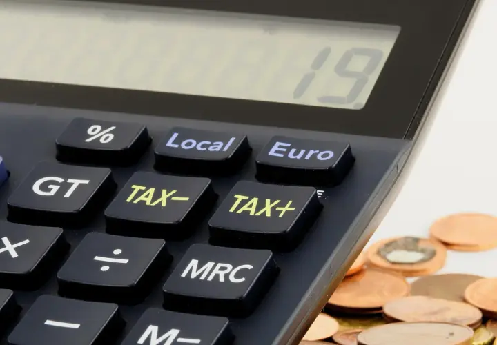 Kalkulator z klawiszami "TAX+", "TAX-" i "Euro" obok stosu monet. Czas na rozliczenie działalności gospodarczej do kiedy?