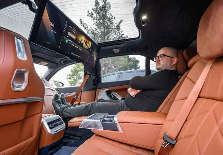 Wnętrze BMW i6 z ekranem multimedialnym dla pasażerów. Mężczyzna relaksuje się na tylnym siedzeniu.