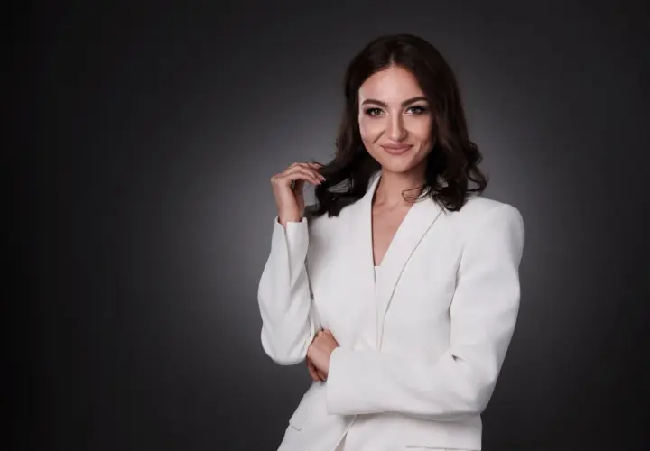 Elegancka kobieta w białej marynarce, uśmiecha się pewnie. To profesjonalne zdjecie biznesowe.