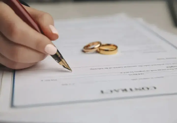 Dłoń z piórem podpisuje dokument, obok leżą obrączki. To umowa o rozdzielność majątkową.