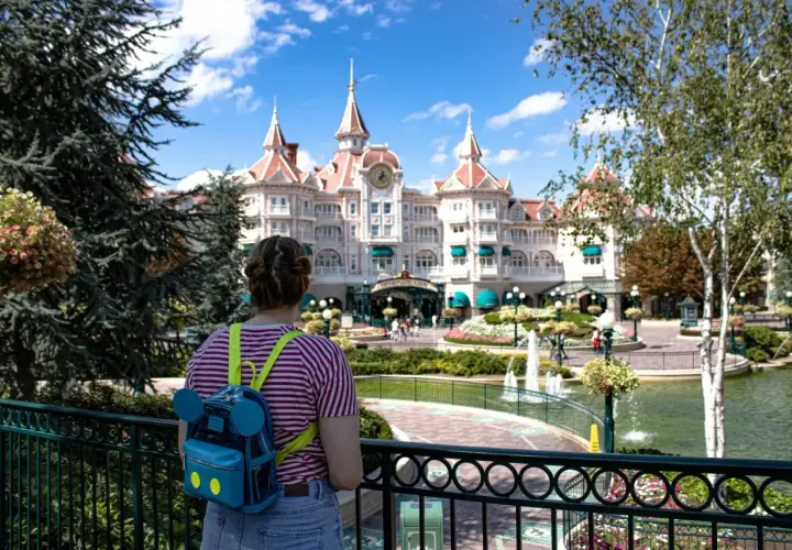 Dziewczyna z plecakiem w kształcie Myszki Miki patrzy na zamek w Disneylandzie. Zastanawia się, ile kosztuje bilet do Disneylandu.