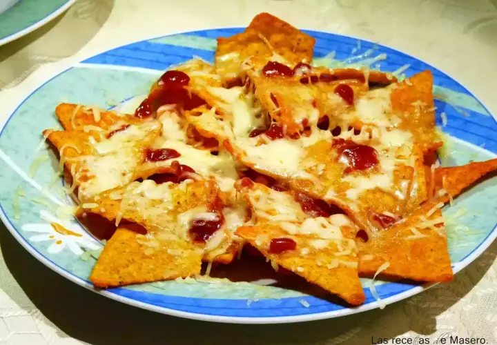 Nachos con queso derretido y salsa roja, servidos en un plato azul y verde. ¡Un antojo irresistible!