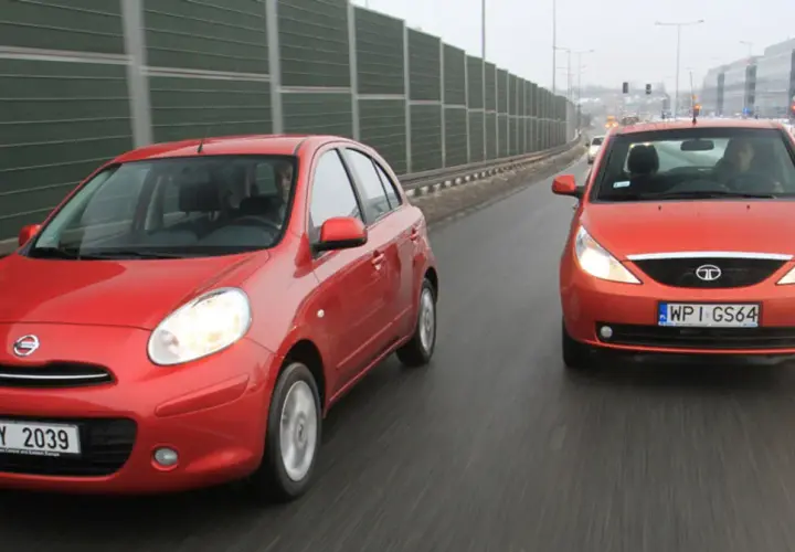 Dwa czerwone samochody, Nissan i tata indica, jadą obok siebie po mokrej drodze.