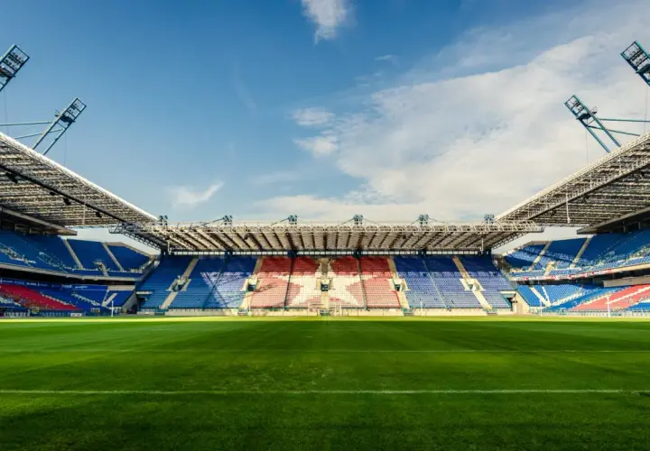 Pusta trybuna stadionu Wisły Kraków, z niebieskimi i czerwonymi siedzeniami tworzącymi wzór gwiazdy. Pojemność stadionu robi wrażenie.