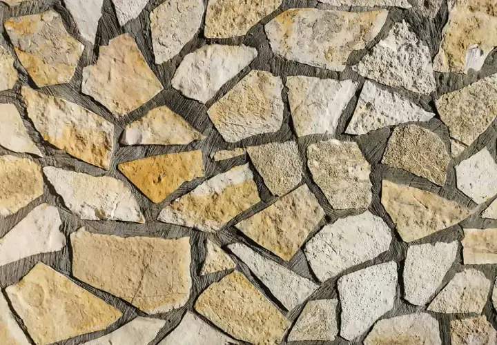 Kamienna ściana z nieregularnych, żółtawych i białych kamieni. Piaskowiec tworzy naturalną, rustykalną mozaikę.
