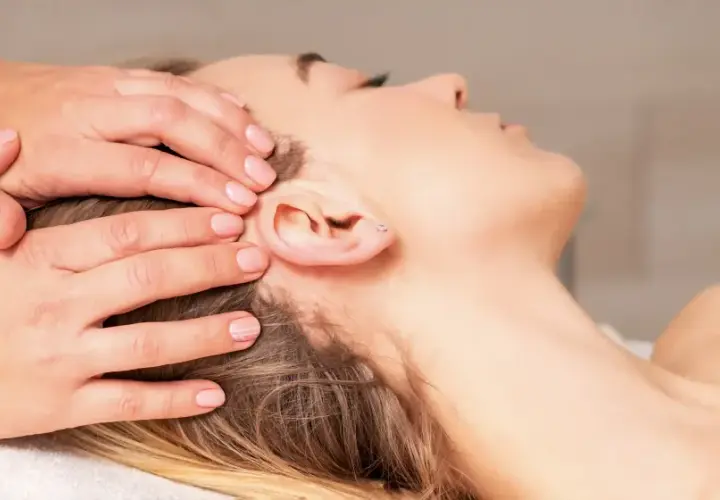 Mains douces appliquant une thérapie cranio sacrée sur la tête d'une femme détendue.