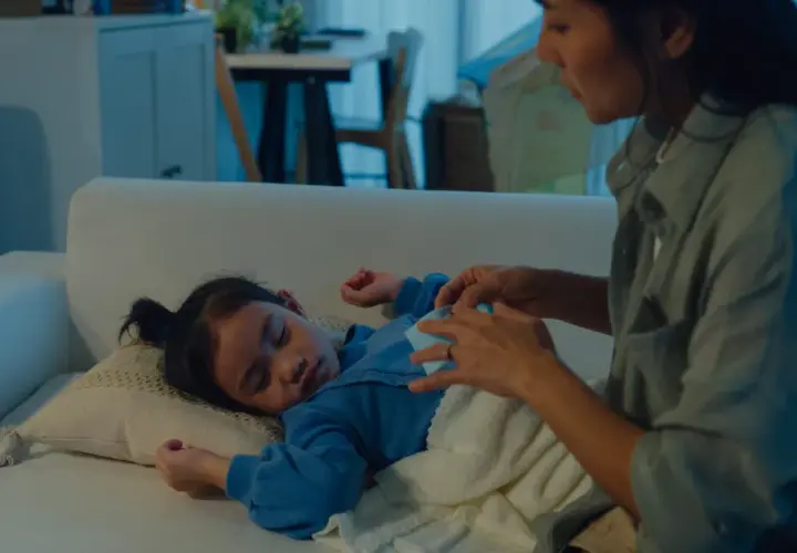 Mamma accarezza dolcemente il suo bambino che dorme sul divano, uno dei tanti bambini che si svegliano di notte.