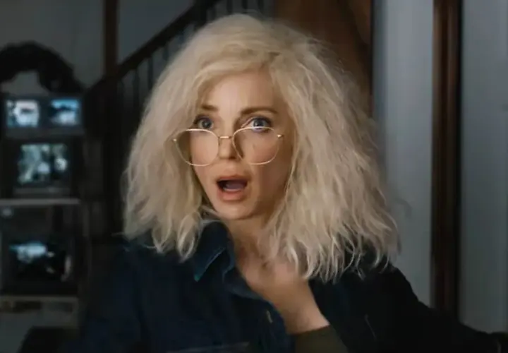 Kobieta z blond włosami i okularami, przerażona, jakby oglądała straszny film 6. W tle monitory.