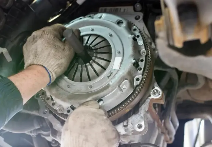 Mechanik w rękawiczkach naprawia sprzęgło samochodowe.