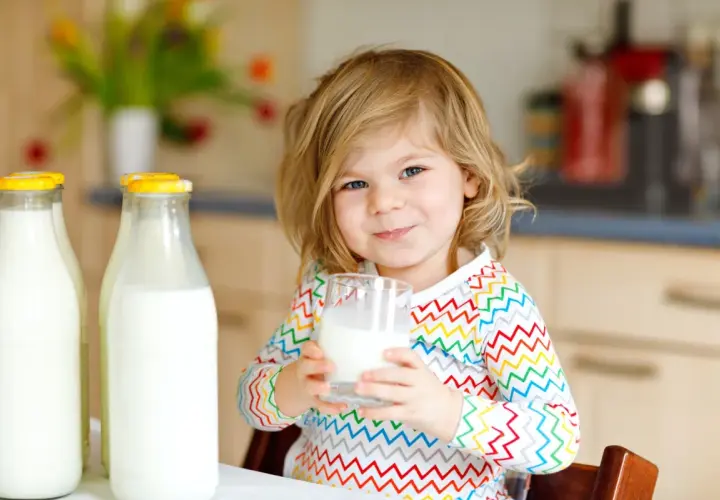 Bambina sorridente con bicchiere di latte vaccino cos'è. Due bottiglie di latte fresco sul tavolo.