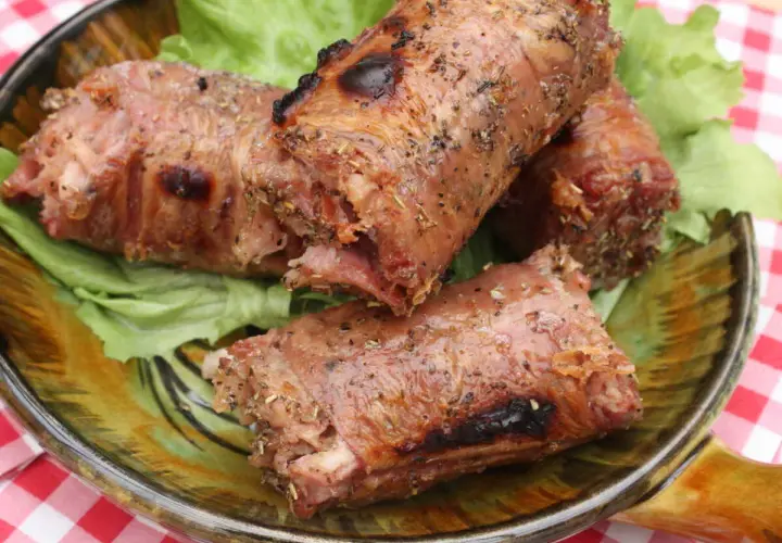 Trois andouillettes grillées au barbecue, servies sur un lit de laitue dans une assiette décorative.