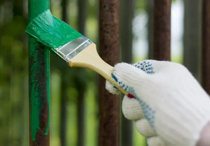 Mano guantata stende vernice verde su un palo di ferro arrugginito. La temperatura ideale per verniciare il ferro è fondamentale per una buona resa.