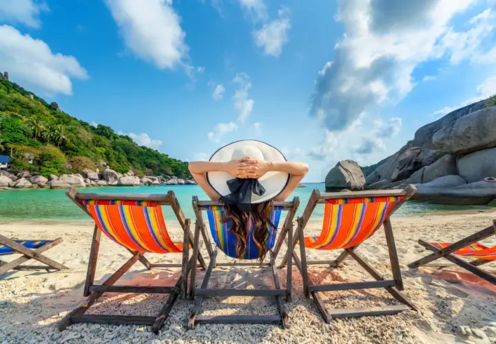 Kobieta w kapeluszu odpoczywa na leżaku na tropikalnej plaży.