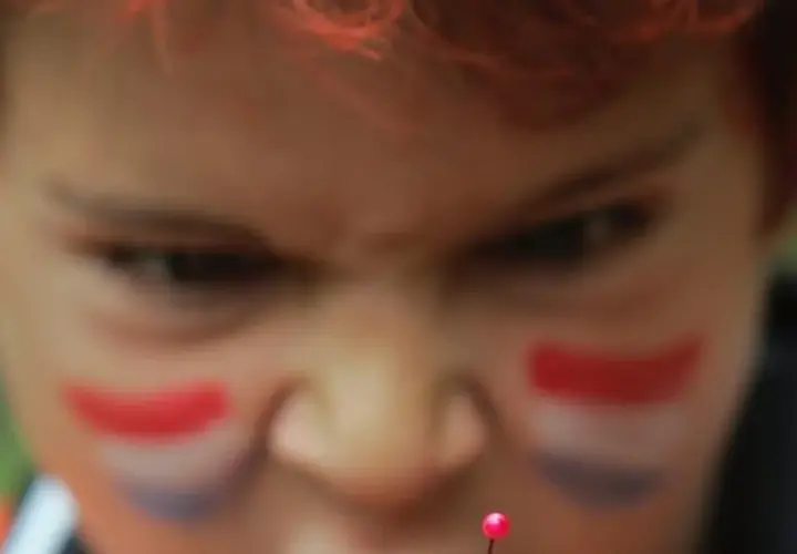 Niño con pintura facial de bandera, con mirada intensa, como si temiera el mal de ojo.