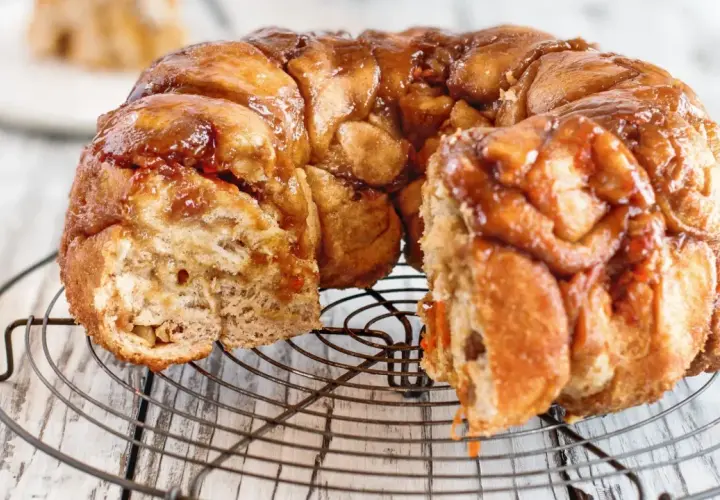 Pyszny, karmelizowany monkey bread przepis na okrągłej kratce. Ciasto jest lekko rozwarstwione, z widocznymi kawałkami ciasta.