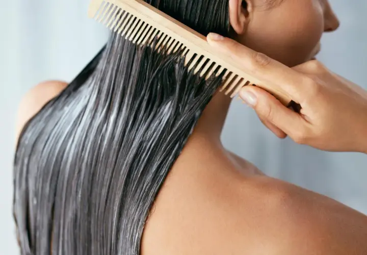 Persona peina su cabello oscuro con mascarilla y un peine de madera. Averigua cuanto tiempo dejar la mascarilla en el pelo para un tratamiento óptimo.