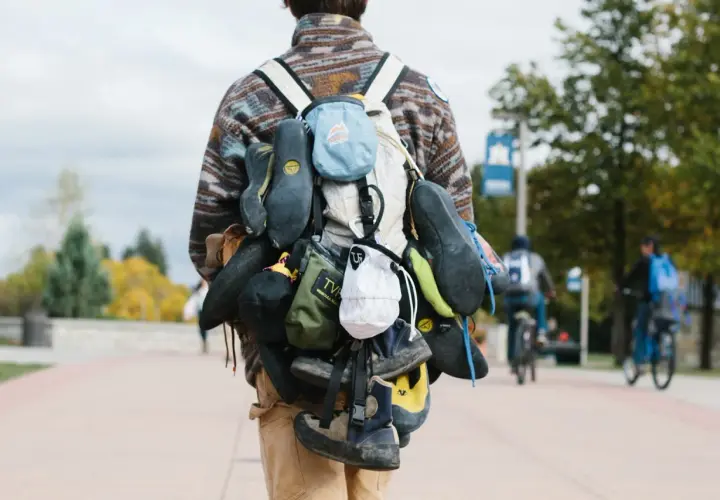 A climber's backpack is laden with multiple pairs of climbing shoes, a testament to a day of ascents.