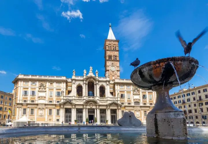La basilique Sainte-Marie-Majeure se dresse fièrement sous un ciel bleu, avec une fontaine et des pigeons au premier plan.