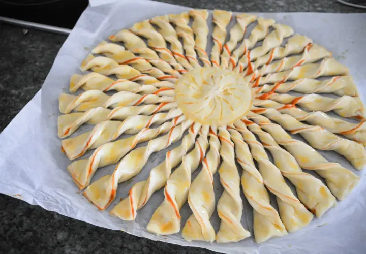 Tarte soleil prête à cuire, avec sa pâte feuilletée torsadée et son centre décoré. Un délice visuel et gustatif.