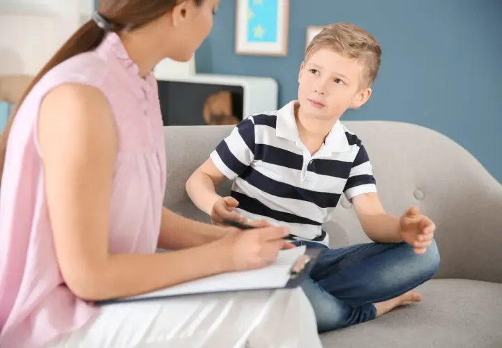 Psycholog rozmawia z chłopcem siedzącym na kanapie.