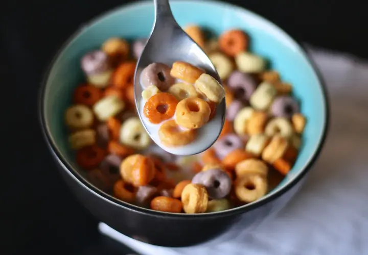 Kolorowe kółeczka płatków śniadaniowych w mleku, nabierane łyżką. Pyszny, kolorowy cereal po polsku na śniadanie.