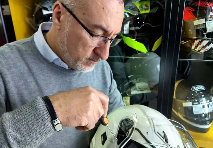 Uomo con cacciavite regola la visiera di un casco bianco, assicurandosi che il casco debba avere la visiera priva di graffi.