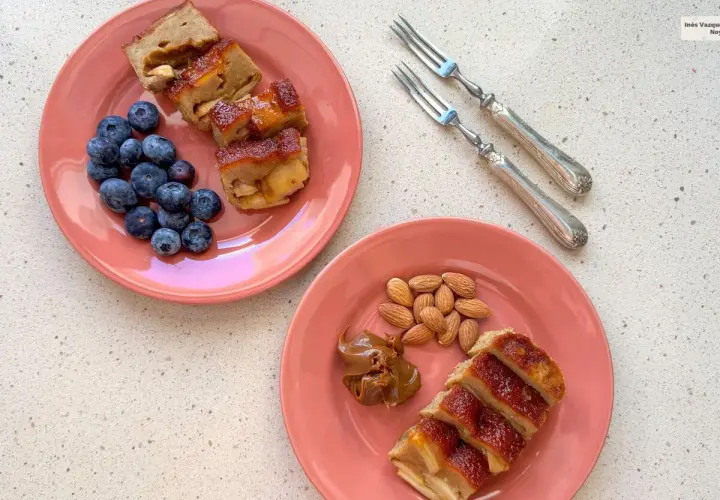 Dos platos rosados con porciones de pudin de manzana, arándanos y almendras. Un postre casero para disfrutar.