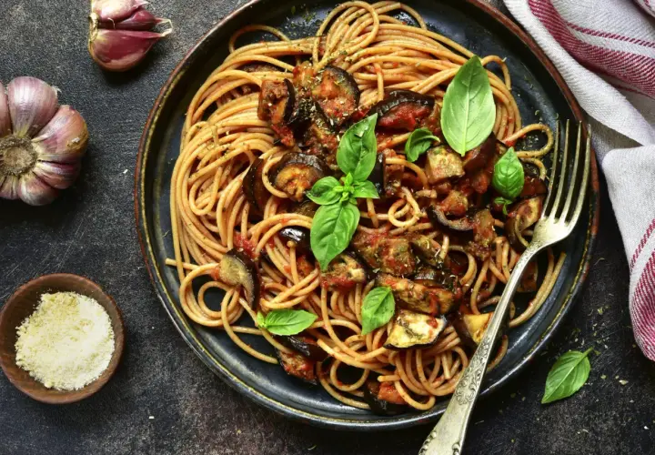 Assiette de pâtes à l'italienne, spaghetti avec aubergines et sauce tomate, garnie de basilic frais. Ail et parmesan à côté.