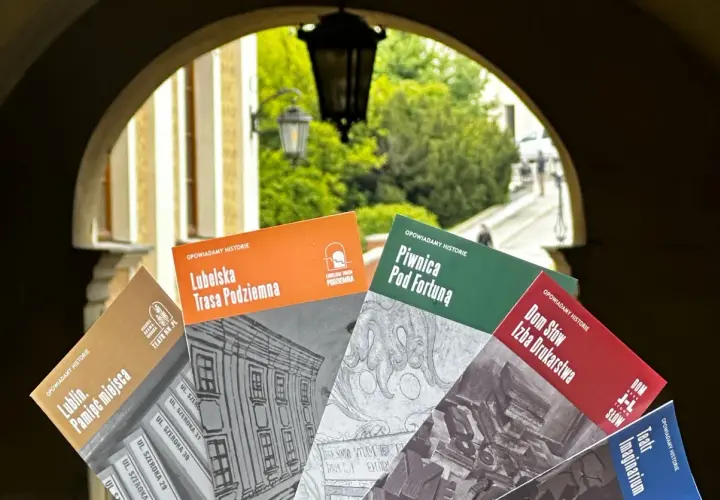 Książki o historii Lublina, m.in. "Lubelska Trasa Podziemna" i "Piwnica Pod Fortuną", prezentowane na tle bramy. Teatr NN Lublin zaprasza do odkrywania przeszłości.