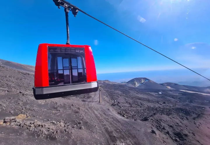 Cabina rossa della funivia in viaggio verso l'altezza Etna Rifugio Sapienza, su un paesaggio lunare di rocce laviche.