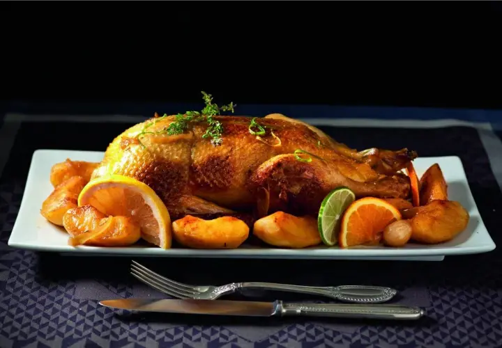 Canard rôti, pommes caramélisées et agrumes en accompagnement. Une canette dorée, prête à être dégustée.