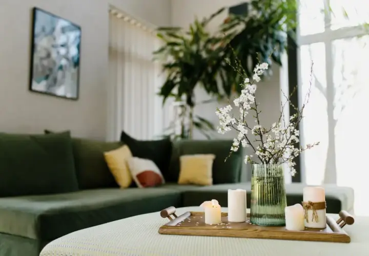Stolik z świecami i gałązką kwitnącej wiśni, zielona kanapa w tle. Aranżacja zgodna z zasadami feng shui, wprowadzająca harmonię.