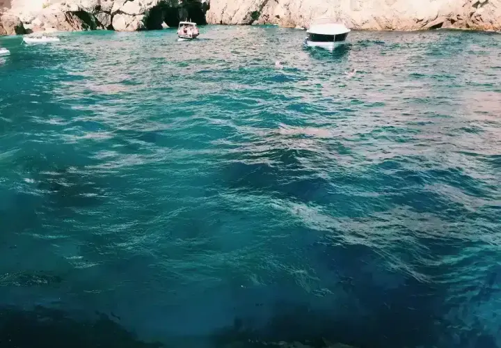 Acqua cristallina e turchese vicino all'ingresso di una grotta, con barche e bagnanti che godono della bellezza della Grotta Azzurra.