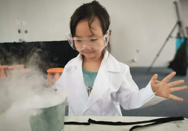 Niña con bata de científico y gafas experimenta con humo, ¡geniales inventos para niños de 6 a 8 años!