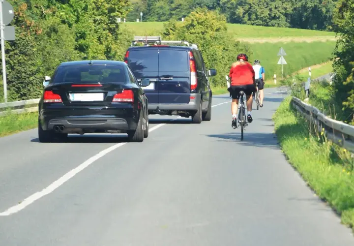 Rowerzyści na drodze, przestrzegający przepisy ruchu drogowego dla rowerzystów, mijani przez samochody i vana.