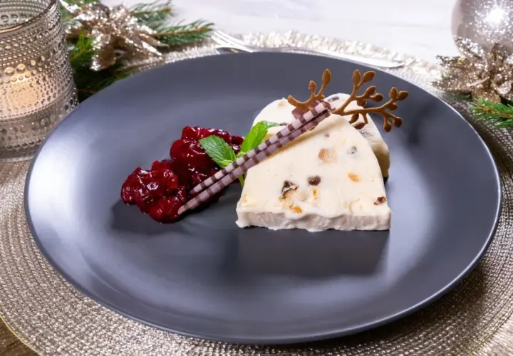 Ein festlicher weihnachts nachtisch: Eisparfait mit Beerenkompott, Schokoladenstäbchen und Rentiergeweih-Dekoration.