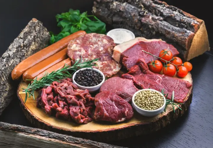 Mięso, kiełbaski, pomidorki i przyprawy na desce. Idealne składniki na dietę karniwora co jeść.
