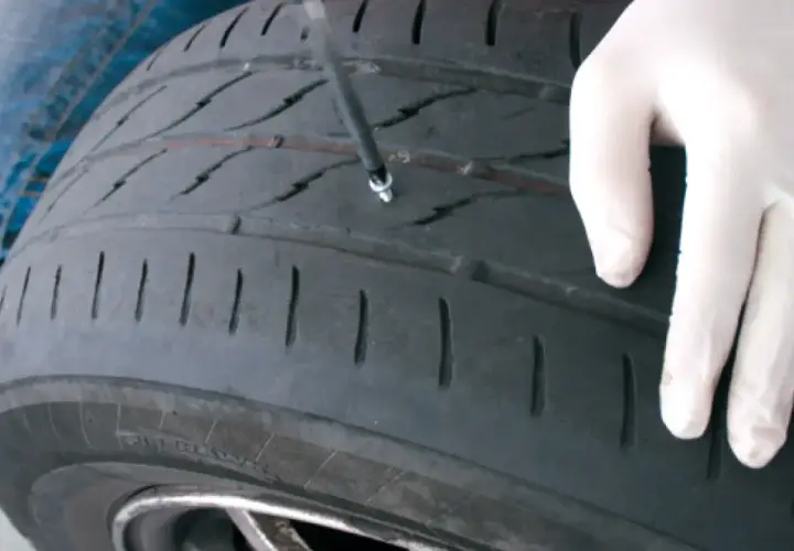 Mano enguantada inserta herramienta para reparar pinchazo. Es seguro reparar un pinchazo si se hace correctamente.