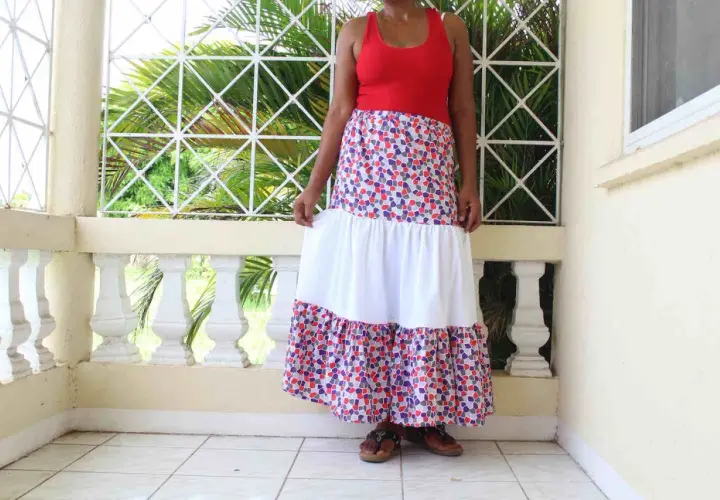 A woman models a long, tiered skirt with a colorful, mosaic-like pattern. The skirt features a white middle tier, creating a flowing, bohemian look.