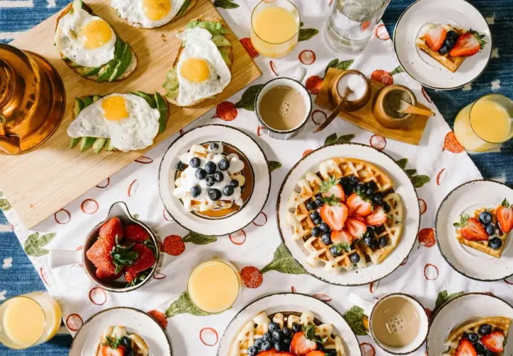 Un festin de brunch : toasts à l'avocat et œuf au plat, gaufres aux fruits rouges et myrtilles, jus d'orange et café.