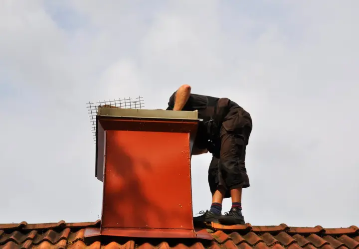 Pracownik na dachu sprawdza komin. Dowiedz się, ile kosztuje naprawa komina na dachu, gdy wymaga prac wysokościowych.