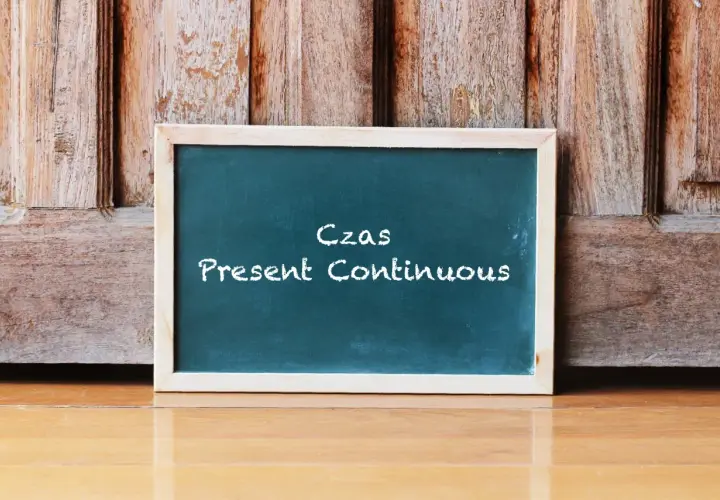 Tablica z napisem "Czas Present Continuous" na tle drewnianych drzwi. Uczysz się, co to jest present continuous?