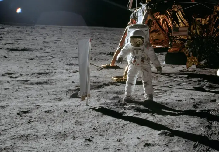 Astronaut na Księżycu podczas misji Apollo, obok lądownika. W tle amerykańska flaga.