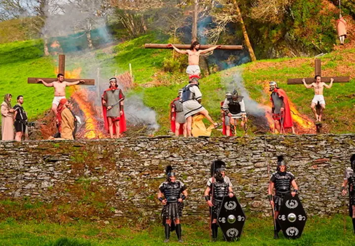 Recreación de la crucifixión en Semana Santa en Asturias. Hombres vestidos de romanos y figuras crucificadas en un paisaje verde.