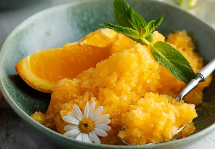 Pomarańczowy sorbet w misce z plasterkiem pomarańczy, miętą i kwiatkiem.
