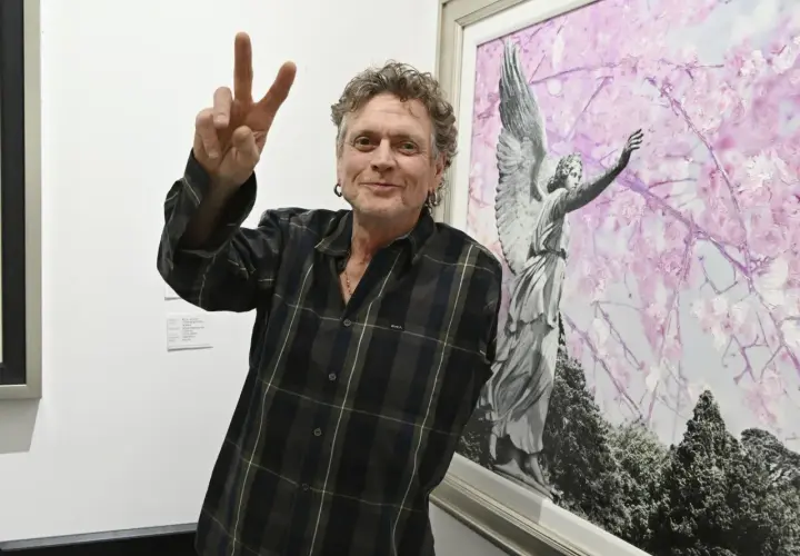 Rick Allen, perkusista Def Leppard, pozuje z uniesionym znakiem pokoju obok obrazu z aniołem i kwitnącymi drzewami.