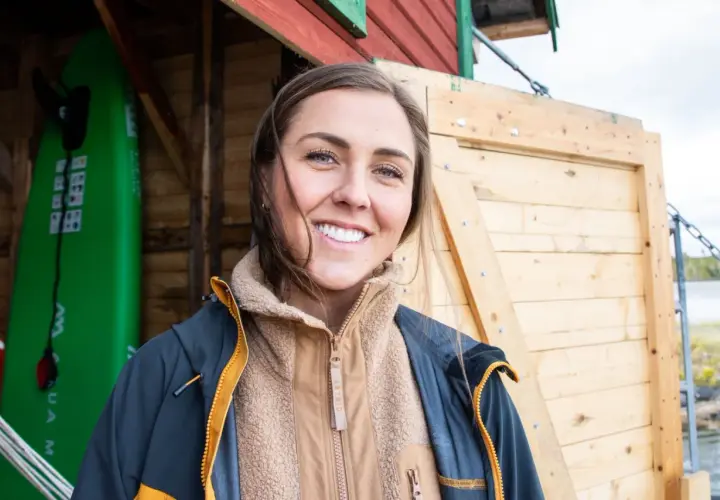 Amanda Robinson ler glatt framför en grön surfbräda och en träbyggnad.