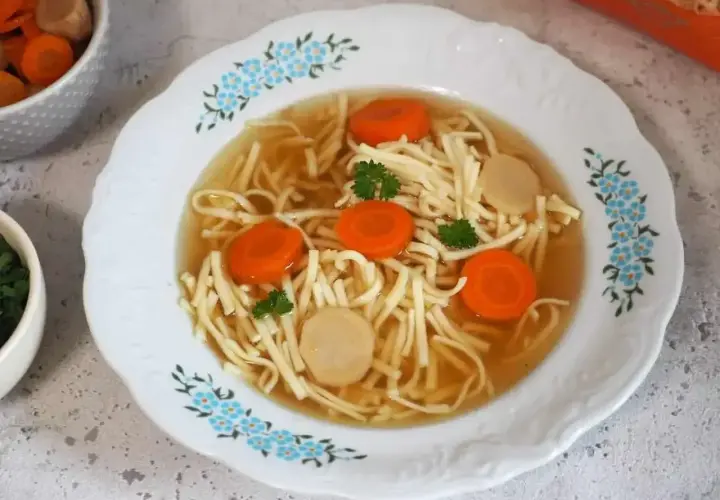 Aksamitny rosół z kaczki z makaronem, marchewką i kawałkami mięsa, ozdobiony natką pietruszki.