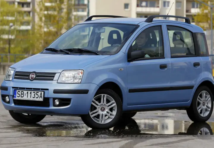 Niebieski Fiat Panda z kierowcą, stojący na mokrej nawierzchni. Kierowca zastanawia się nad aktualną ceną gazu.