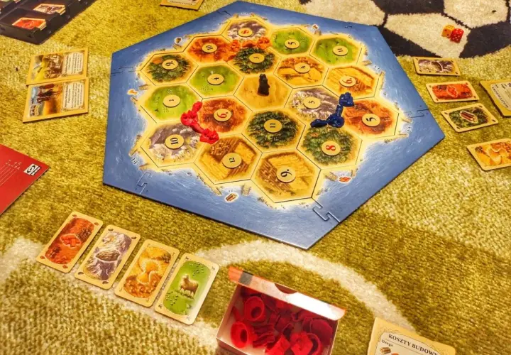 Catan wersja podróżna na dywanie. Plansza z wyspą, karty surowców i pionki.